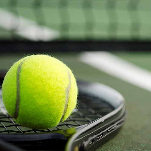 tennis ball balanced on a tennis racket in front of a tennis net